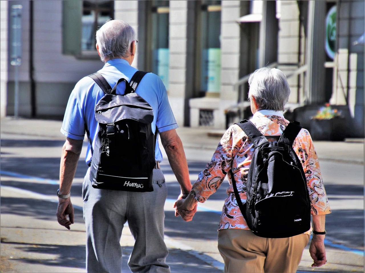 Couple de personnes âgées souriant, portant des sacs à dos, en extérieur