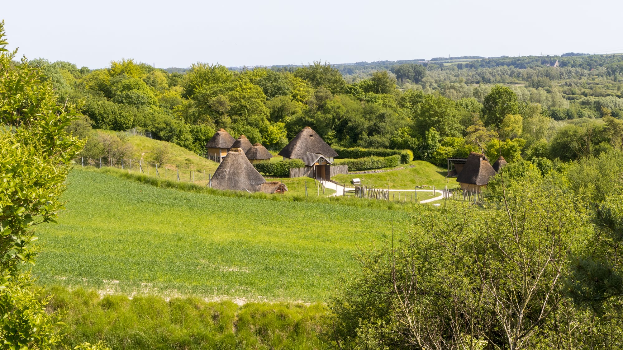 Vue panoramique du village gaulois reconstitué à l'Archéosite de Samara (Somme) — maisons rondes au toit de chaume, palissade en bois, terrains ouverts